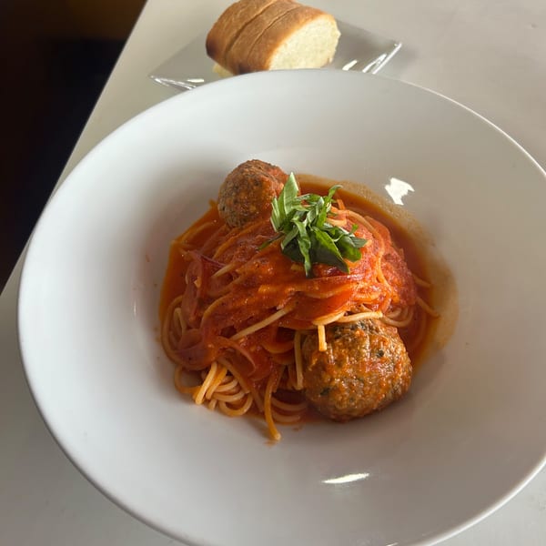 Spaghetti and meatballs with tomato sauce and fresh basil, served with a side of bread.