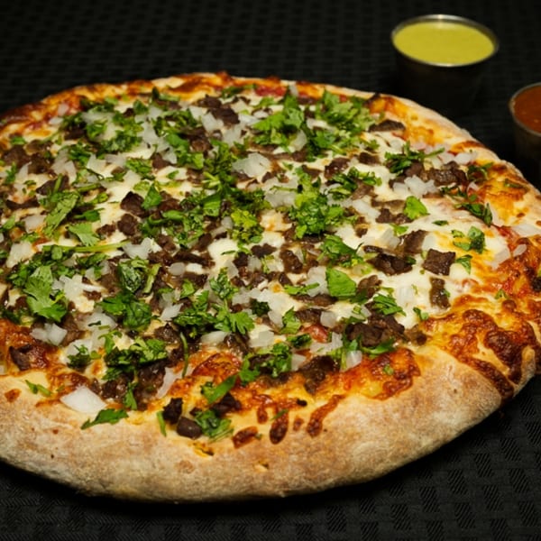 Finas Trattoria's pizza with beef, onions, and cilantro, with two dipping sauces in the background.