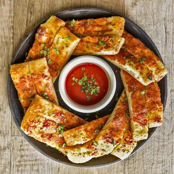 Finas Trattoria's cheesy breadsticks with marinara dipping sauce, garnished with fresh parsley.